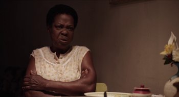 An older woman sitting at a table with her arms crossed