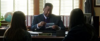 Movie still from “Bad Moms” (2016), directed by Scott Moore – A man sitting at a desk looking at a piece of paper; Close Up shot, Over the shoulder angle