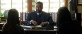 Movie still from “Bad Moms” (2016), directed by Scott Moore – A man sitting at a desk in front of papers; Medium shot, Over the shoulder angle