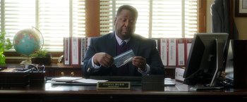 Movie still from “Bad Moms” (2016), directed by Scott Moore – A man sitting at a desk holding a piece of paper in front of him; Close Up shot, Over the shoulder angle