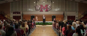 Movie still from “Bad Moms” (2016), directed by Scott Moore – A man standing at a podium in front of an audience; Extreme Wide shot, High angle