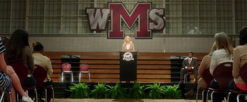 Movie still from “Bad Moms” (2016), directed by Scott Moore – A woman standing at a podium in front of a building; Extreme Wide shot, Low angle