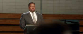 Movie still from “Bad Moms” (2016), directed by Scott Moore – A man standing at a podium in front of a microphone; Close Up shot, Over the shoulder angle