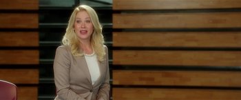 Movie still from “Bad Moms” (2016), directed by Scott Moore – A blonde woman in a brown suit smiling for the camera; Medium shot, Low angle