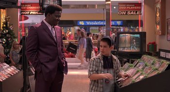 Movie still from “Bad Santa” (2003), directed by Terry Zwigoff – A man in a suit talking to a boy in a checkered shirt; Wide shot, Over the shoulder angle