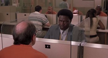 Movie still from “Bad Santa” (2003), directed by Terry Zwigoff – A man in a gray suit is talking to another man in an orange shirt; Medium shot, Over the shoulder angle