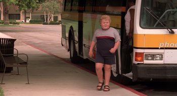 Movie still from “Bad Santa” (2003), directed by Terry Zwigoff – A young boy standing next to a bus on the side of the road; Wide shot, Low angle
