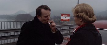Movie still from “Bad Timing: A Sensual Obsession” (1980), directed by Nicolas Roeg – A man smoking a cigarette while talking to a woman on the side of the road; Medium shot, Over the shoulder angle