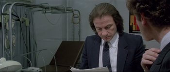 Movie still from “Bad Timing: A Sensual Obsession” (1980), directed by Nicolas Roeg – A man sitting at a desk reading a paper; Close Up shot, Low angle