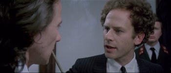 Movie still from “Bad Timing: A Sensual Obsession” (1980), directed by Nicolas Roeg – A man in a suit smoking a cigarette next to another man in a suit and tie; Close Up shot, Over the shoulder angle