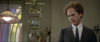 Movie still from “Bad Timing: A Sensual Obsession” (1980), directed by Nicolas Roeg – A man in a suit standing in front of a shelf; Close Up shot, Over the shoulder angle