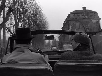 Movie still from “Band of Outsiders” (1964), directed by Jean-Luc Godard – Two men are driving in the back of a car; Wide shot, High angle
