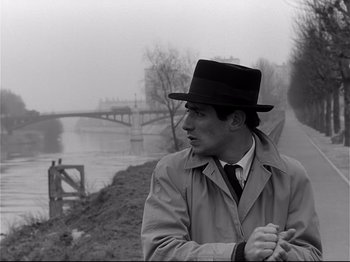 Movie still from “Band of Outsiders” (1964), directed by Jean-Luc Godard – A black and white photo of a man wearing a hat; Medium shot, Over the shoulder angle