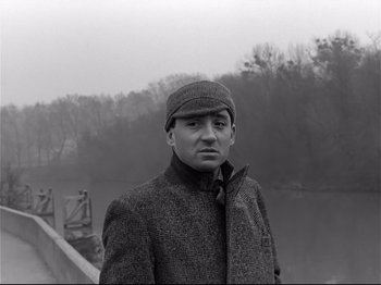 Movie still from “Band of Outsiders” (1964), directed by Jean-Luc Godard – A black and white photo of a man wearing a coat and hat; Close Up shot, Low angle