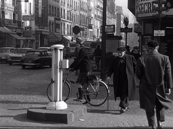 Movie still from “Band of Outsiders” (1964), directed by Jean-Luc Godard – An old black and white photo of a man riding a bike; Wide shot, High angle