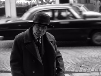 Movie still from “Band of Outsiders” (1964), directed by Jean-Luc Godard – A black and white photo of a man wearing a hat; Medium shot, Over the shoulder angle