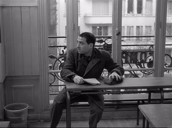 Movie still from “Band of Outsiders” (1964), directed by Jean-Luc Godard – A black and white photo of a man sitting on a bench; Medium shot, High angle