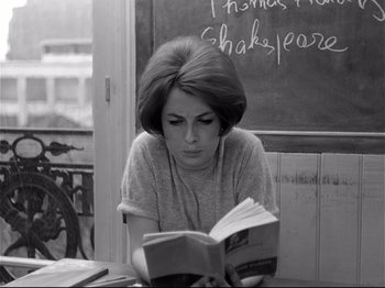 Movie still from “Band of Outsiders” (1964), directed by Jean-Luc Godard – A woman sitting in front of a chalkboard while reading a book; Close Up shot, High angle