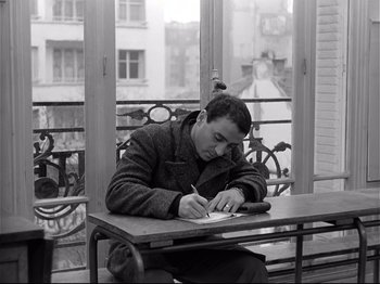 Movie still from “Band of Outsiders” (1964), directed by Jean-Luc Godard – A man sitting at a table writing on a piece of paper; Medium shot, High angle
