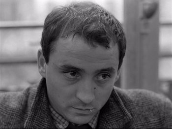 Movie still from “Band of Outsiders” (1964), directed by Jean-Luc Godard – Black and white photograph of a young man with a serious look on his face; Close Up shot, High angle