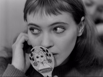 Movie still from “Band of Outsiders” (1964), directed by Jean-Luc Godard – A woman holding a wooden spoon with a picture of a girl on it in front of her face; Close Up shot, High angle