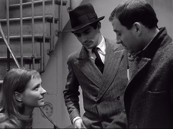 Movie still from “Band of Outsiders” (1964), directed by Jean-Luc Godard – Two men and a woman standing next to each other; Medium shot, Over the shoulder angle