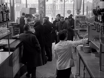 Movie still from “Band of Outsiders” (1964), directed by Jean-Luc Godard – A group of people standing around a restaurant; Wide shot, High angle