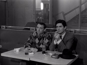 Movie still from “Band of Outsiders” (1964), directed by Jean-Luc Godard – A couple of men sitting at a table in front of a window; Medium shot, High angle