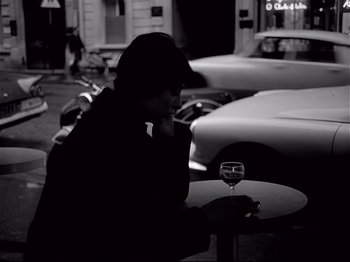 Movie still from “Band of Outsiders” (1964), directed by Jean-Luc Godard – A man sitting at a table with a glass of wine; Medium shot, High angle