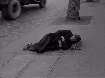 Movie still from “Band of Outsiders” (1964), directed by Jean-Luc Godard – A man laying on the ground on the sidewalk; Wide shot, High angle