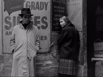 Movie still from “Band of Outsiders” (1964), directed by Jean-Luc Godard – A man and a woman standing in front of a building; Medium shot, Low angle