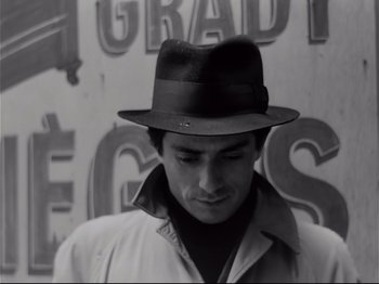 Movie still from “Band of Outsiders” (1964), directed by Jean-Luc Godard – A man wearing a hat standing in front of a wall; Close Up shot, Low angle