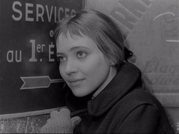 Movie still from “Band of Outsiders” (1964), directed by Jean-Luc Godard – A young woman standing in front of a sign; Close Up shot, High angle