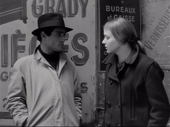 Movie still from “Band of Outsiders” (1964), directed by Jean-Luc Godard – A man and a woman standing next to each other on the street; Close Up shot, Over the shoulder angle