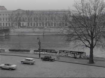 Movie still from “Band of Outsiders” (1964), directed by Jean-Luc Godard – A black and white photo of a street with cars driving down it; Extreme Wide shot, High angle