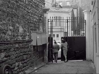 Movie still from “Band of Outsiders” (1964), directed by Jean-Luc Godard – Two people are walking down the street in a black and white photo; Wide shot, High angle