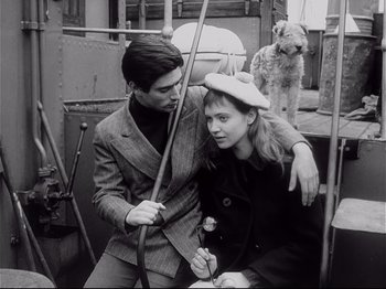 Movie still from “Band of Outsiders” (1964), directed by Jean-Luc Godard – A man and a woman sitting on a bus with a dog in the background; Medium shot, High angle