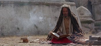 Movie still from “Baraka” (1992), directed by Ron Fricke – A man with dreadlocks sitting on the ground reading a book; Medium shot, Low angle