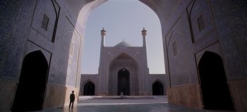 Movie still from “Baraka” (1992), directed by Ron Fricke – A man is standing in front of a building with arches; Extreme Wide shot, Low angle