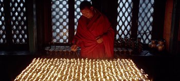Movie still from “Baraka” (1992), directed by Ron Fricke – A man in a red robe lighting a candle; Wide shot, High angle