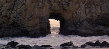 Movie still from “Baraka” (1992), directed by Ron Fricke – A view of the ocean through a rock arch at sunset; Extreme Wide shot, High angle