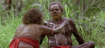 Movie still from “Baraka” (1992), directed by Ron Fricke – A man is painting another man's face with white paint; Medium shot, Over the shoulder angle