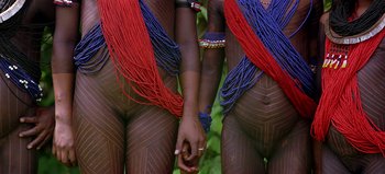 Movie still from “Baraka” (1992), directed by Ron Fricke – Two people holding hands with blue and red beads; Medium shot, Overhead angle