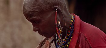 Movie still from “Baraka” (1992), directed by Ron Fricke – An older man wearing a lot of beads and ear hangers; Close Up shot, Over the shoulder angle