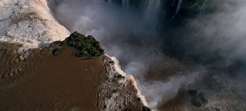 Movie still from “Baraka” (1992), directed by Ron Fricke – A view of a body of water and a waterfall from above; Extreme Wide shot, High angle