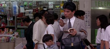 Movie still from “Baraka” (1992), directed by Ron Fricke – A man in a suit and tie looking at his cell phone; Medium shot, Low angle