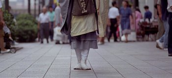 Movie still from “Baraka” (1992), directed by Ron Fricke – A person walking down a street with a bag on his back; Wide shot, Low angle