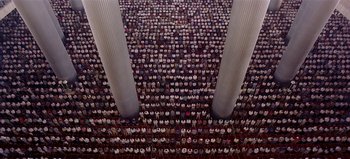 Movie still from “Baraka” (1992), directed by Ron Fricke – A room filled with lots of people standing in front of pillars; Extreme Wide shot, Overhead angle