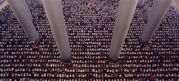 Movie still from “Baraka” (1992), directed by Ron Fricke – A large group of people sitting in front of pillars; Extreme Wide shot, Overhead angle