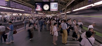Movie still from “Baraka” (1992), directed by Ron Fricke – A crowd of people standing in a train station next to a clock; Extreme Wide shot, High angle